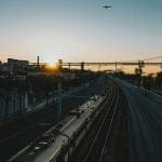 Train going down the tracks with an airplane appearing in the sky.