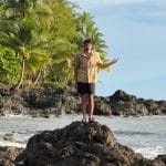 Ben Kielesinski photographed standing on a rock on the shore of Costa Rica, gesturing to the landscape around him.